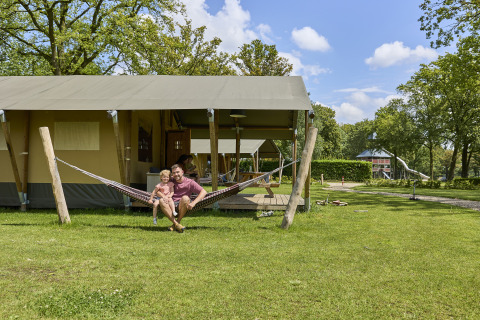 Gezin in hangmat voor een luxe glamping safaritent bij De Leistert, Nederland, geniet van hun vakantie.