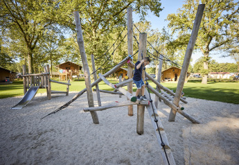Niño jugando en parque de escalada en Glamping Tent Luxe, De Leistert, Países Bajos, rodeado de naturaleza.