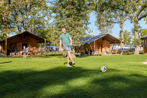 Mann spielt Fußball auf Rasen vor luxuriösen Safarizelten bei Glamping Tent Luxe in De Leistert.