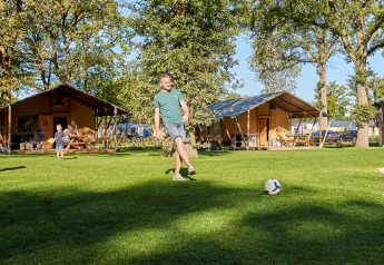Mand sparker bold på græsplæne foran luksuriøse safaritelte ved Glamping Tent Luxe på De Leistert.