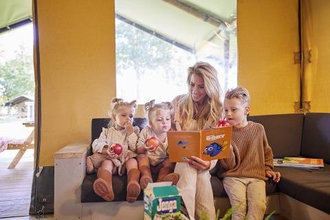 Familie entspannt sich in einem Glamping Tent Luxe bei De Leistert, Niederlande, beim Lesen und Essen.