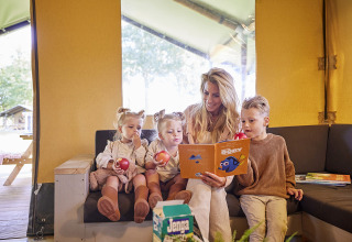 Famiglia che si gode del tempo insieme nella Glamping Tent Luxe a De Leistert, Olanda, leggendo e mangiando mele.