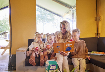 Familia disfruta junta en la Glamping Tent Luxe de De Leistert, Países Bajos, leyendo y comiendo manzanas.
