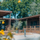 Vista esterna della Luxury Lodge con veranda in legno, circondata da alberi verdi e fiori gialli.
