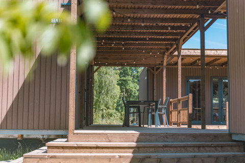 Terraza de madera con pérgola y asientos en Luxury Lodge, rodeada de naturaleza y árboles verdes.