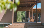 Houten terras met pergola en zitplaatsen bij Luxury Lodge, omgeven door groene natuur en bomen.