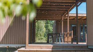 Holzterrasse mit Pergola und Sitzbereich im Luxury Lodge, umgeben von Bäumen und Natur im Sommer.