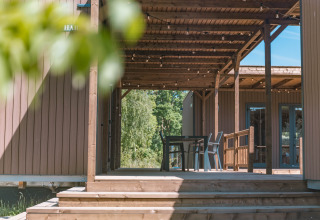 Terraza de madera con pérgola y asientos en Luxury Lodge, rodeada de naturaleza y árboles verdes.