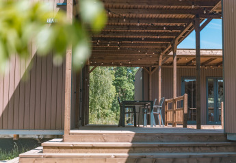 Udendørs træterrasse ved Luxury Lodge med borde og stole under en pergola, omgivet af natur.