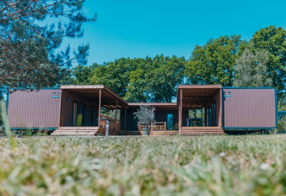 Lujosa cabaña en Holiday Park Sallandshoeve, Países Bajos, rodeada de árboles y césped bajo el cielo azul.