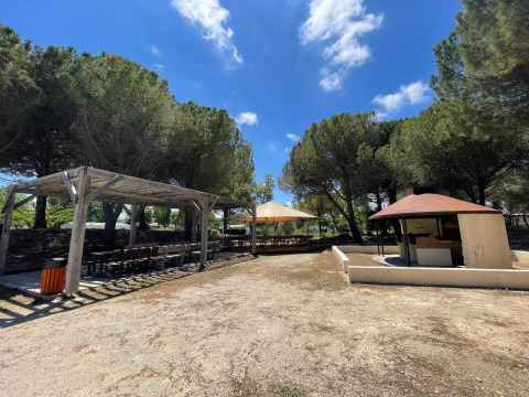 Outdoor picnic area with wooden pergola, barbecue grill, and tables under pine trees at Camping Seasonova Ensoya.
