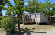 Cabaña llamada Cottage en Camping Seasonova Ensoya en Francia, rodeada de árboles y cielo azul.