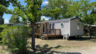 Cabaña llamada Cottage en Camping Seasonova Ensoya en Francia, rodeada de árboles y cielo azul.