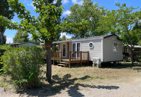 Cabaña llamada Cottage en Camping Seasonova Ensoya en Francia, rodeada de árboles y cielo azul.