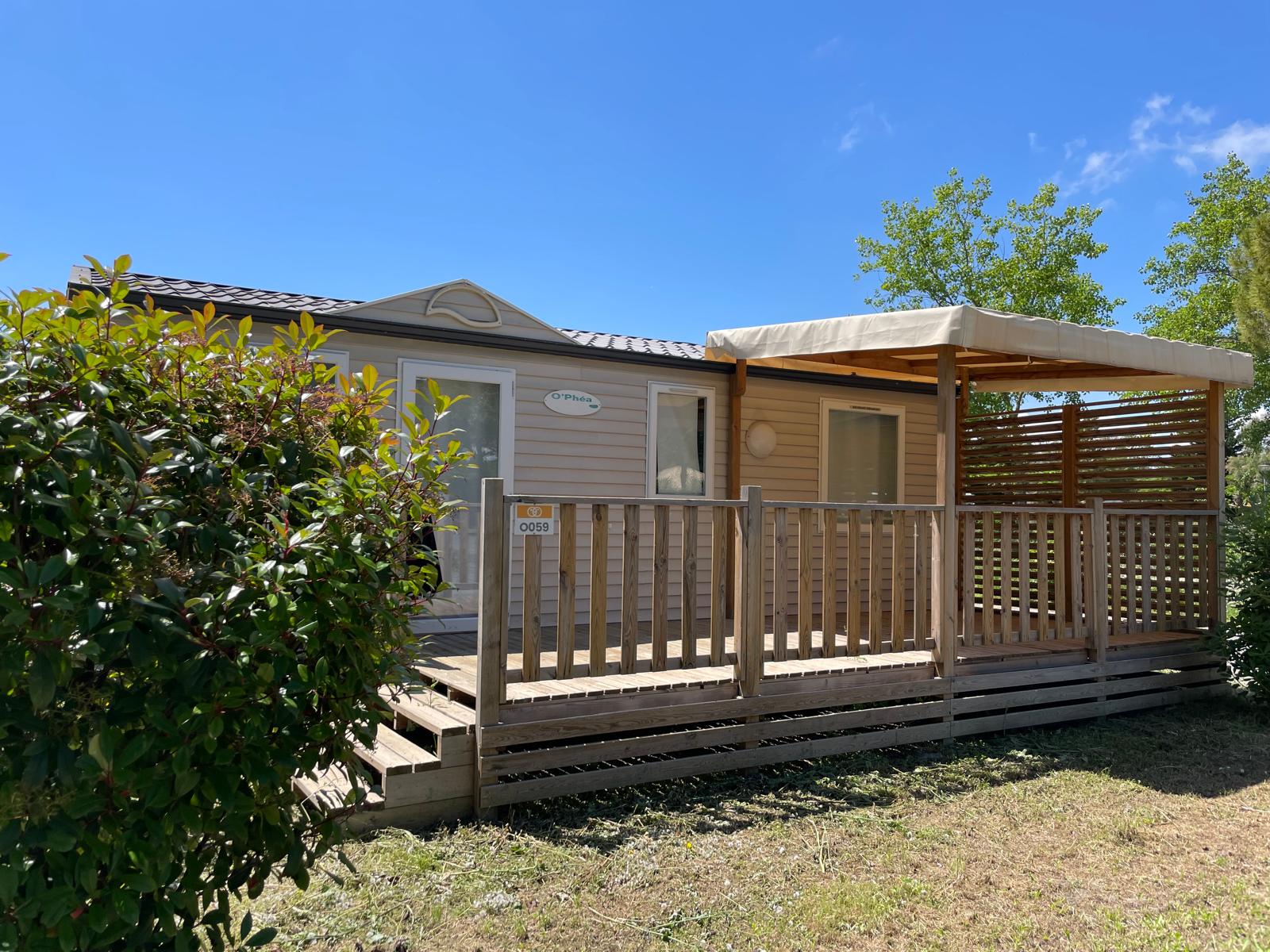 Buitenaanzicht van een Cottage-hut bij Camping Seasonova Ensoya in Frankrijk met houten terras en zon.