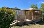 Vista exterior de una cabaña Cottage en Camping Seasonova Ensoya, Francia, con terraza de madera y sol.