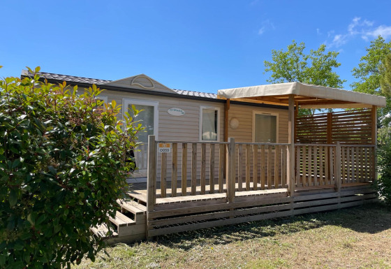 Outdoor view of a Cottage cabin at Camping Seasonova Ensoya in France featuring a wooden deck and sunshine.