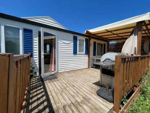 Houten terras met barbecue en overkapping aan een airco-cottage op Camping Seasonova Ensoya, Frankrijk.