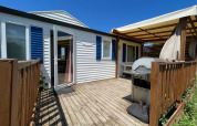 Terraza de madera con barbacoa y toldo en cabaña climatizada en Camping Seasonova Ensoya, Francia.