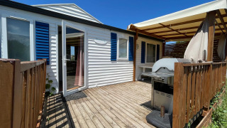 Terraza de madera con barbacoa y toldo en cabaña climatizada en Camping Seasonova Ensoya, Francia.