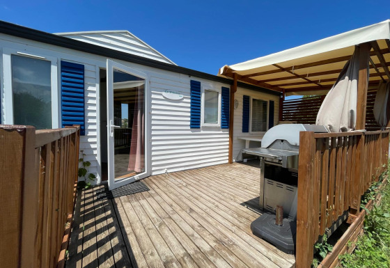 Houten terras met barbecue en zonwering bij een gekoelde cottage op Camping Seasonova Ensoya, Frankrijk.