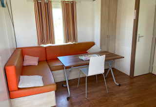 Interieur van een cottage met oranje hoekbank, tafel, stoel en kast bij Camping Seasonova Ensoya in Frankrijk.