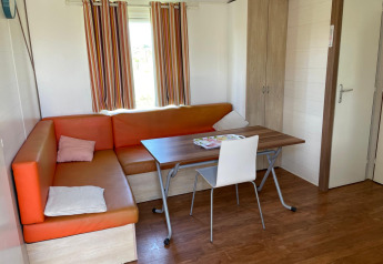 Intérieur d’un cottage avec canapé d’angle orange, table, chaise et armoire au Camping Seasonova Ensoya, France.