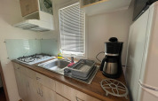 Cabin kitchen with gas stove, sink, coffee maker, and dish rack at Camping Seasonova Ensoya in France.