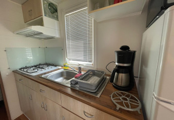Cuisine de cabane avec gazinière, évier, cafetière et égouttoir au Camping Seasonova Ensoya en France.