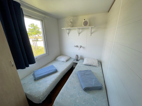 Kleine kamer met twee eenpersoonsbedden, raam, blauwe handdoeken en plank in een Franse vakantiewoning.