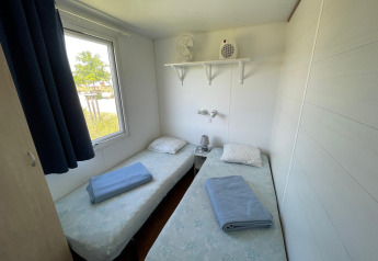 Petite chambre avec deux lits simples, fenêtre, draps bleus, étagère et table de nuit dans un chalet français.