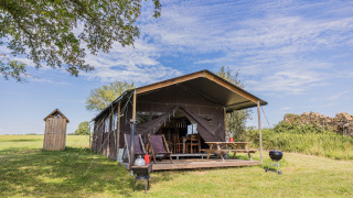 Tienda safari Glampinglodge de luxe con baño privado en un campo verde bajo un cielo azul y despejado.