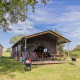 Safari tent Glampinglodge de luxe with private sanitary facilities on a grassy field under blue sky.