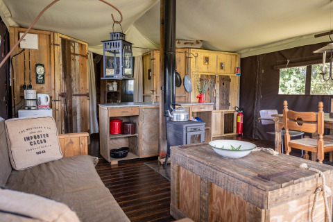 Intérieur d'une tente safari de luxe avec meubles en bois et cuisine au Domaine Bonneblond, France.
