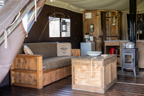 Interieur van een glamping lodge met houten meubels, kachel en gezellige sfeer in Domaine Bonneblond.