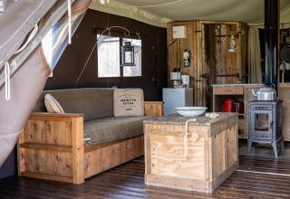 Innenaufnahme eines Glampingzeltes mit Holzmöbeln, Ofen und rustikalem Charme bei Domaine Bonneblond.