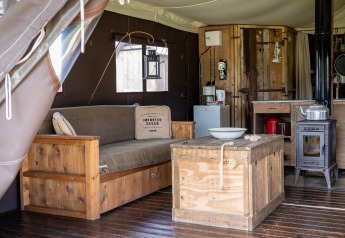 Intérieur d'une tente glamping avec meubles en bois, poêle et déco chaleureuse au Domaine Bonneblond.
