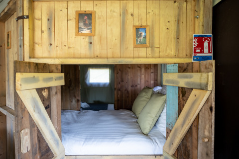 Gezellig houten bed met kussens en dierenfoto’s in Glampinglodge de luxe tent op Domaine Bonneblond.