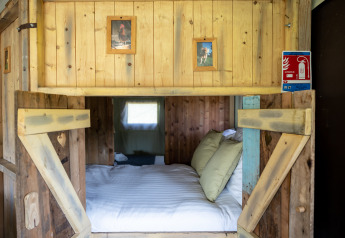 Rustic wooden alcove bed with cozy pillows and animal photos, inside Glampinglodge de luxe in France.