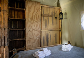 Interior of a safari tent with rustic wooden furniture and towels on the bed at Glampinglodge de luxe in France.