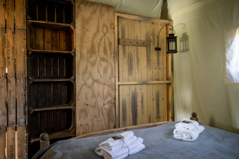 Interno di una tenda safari con mobili rustici e asciugamani sul letto a Glampinglodge de luxe in Francia.