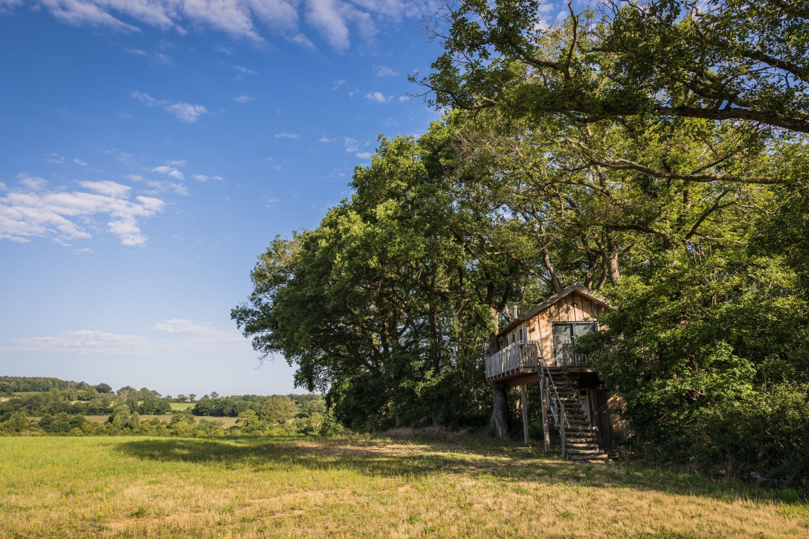 Het Boomhuis op Domaine Bonneblond in Frankrijk, omringd door groene velden en bomen onder een heldere lucht.