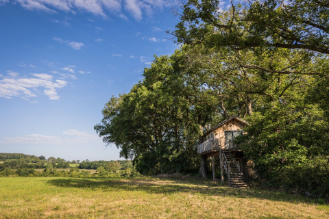 Das Baumhaus Boomhuis auf Domaine Bonneblond in Frankreich, umgeben von Feldern und Bäumen unter blauem Himmel.