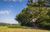 Das Baumhaus Boomhuis auf Domaine Bonneblond in Frankreich, umgeben von Feldern und Bäumen unter blauem Himmel.