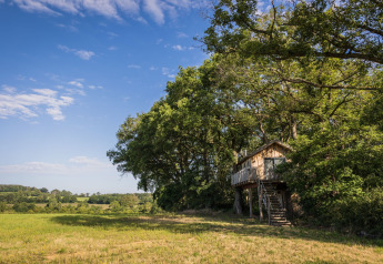 La casa del árbol Boomhuis en Domaine Bonneblond, Francia, rodeada de campos verdes y árboles bajo el cielo azul.