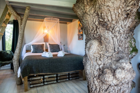 Schlafzimmer in einem einzigartigen Baumhaus bei Domaine Bonneblond, Frankreich, mit Baumstamm und Doppelbett.