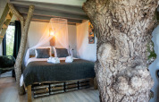 Chambre dans la cabane Boomhuis à Domaine Bonneblond en France, avec troncs d’arbres et lit confortable.