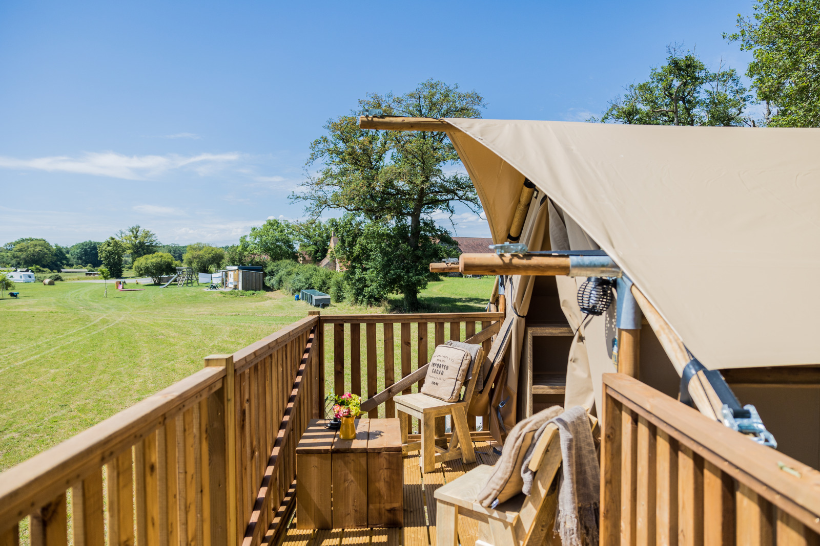 Houten veranda van safaritent Papillon met uitzicht op grasveld, blauwe lucht en zitgelegenheid.