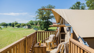 Houten terras bij safaritent Papillon met zicht op groene weide, blauwe lucht en een gezellige zithoek.