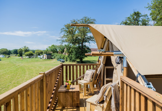 Wooden deck of the Papillon safari tent overlooking a grassy field, blue sky, and relaxing seating area.